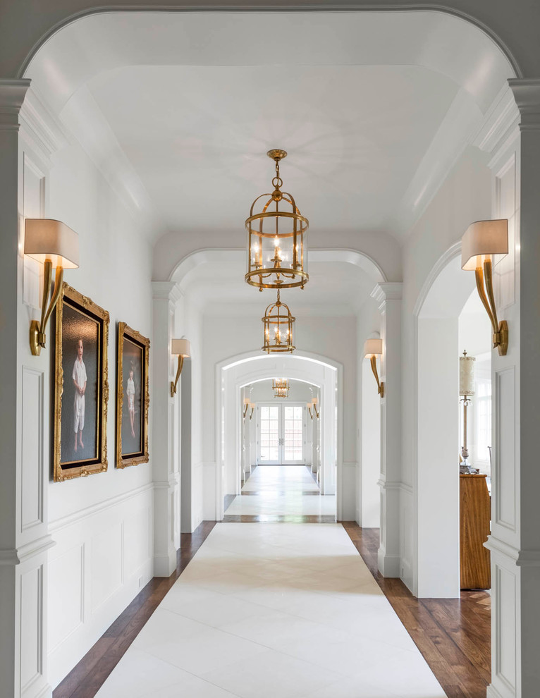 На фото: большой коридор в классическом стиле с белыми стенами и полом из травертина