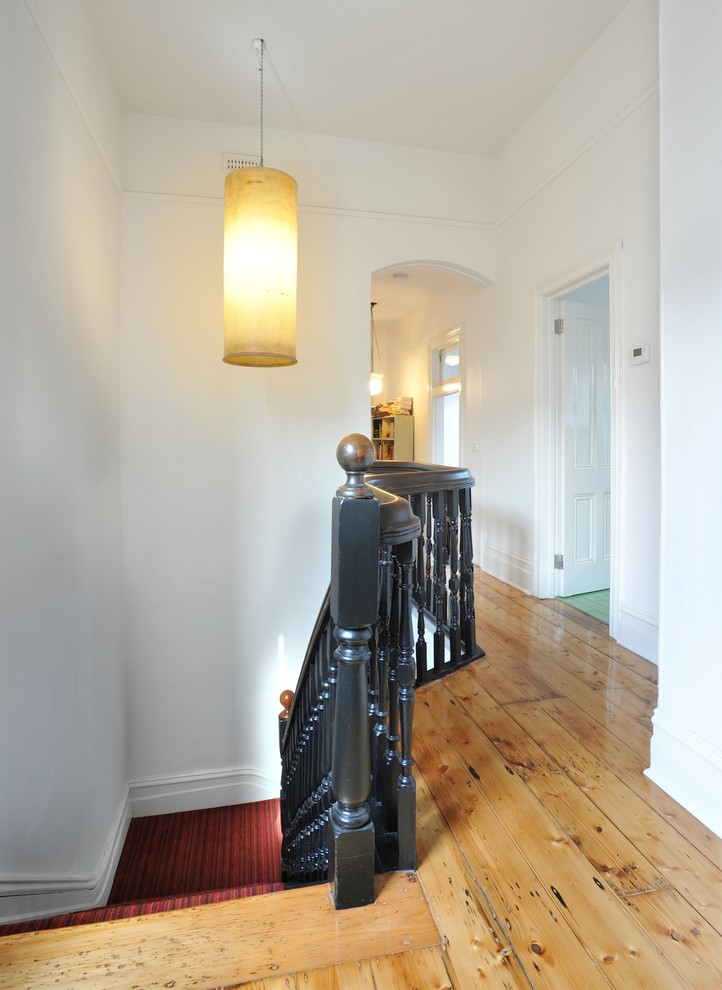 Idée de décoration pour un couloir design avec un mur blanc et un sol en bois brun.