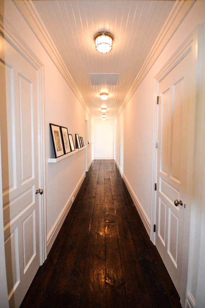 Réalisation d'un grand couloir tradition avec un mur blanc, parquet foncé et un sol marron.
