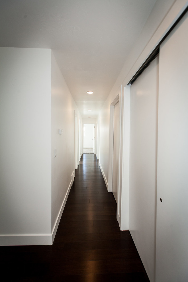 На фото: большой коридор в стиле модернизм с белыми стенами и темным паркетным полом с