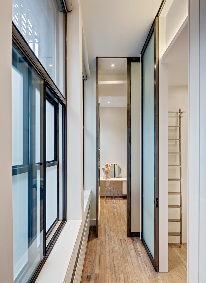 Example of a mid-sized minimalist medium tone wood floor hallway design in New York with white walls