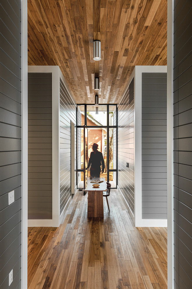 Modelo de recibidores y pasillos minimalistas de tamaño medio con paredes grises, suelo de madera en tonos medios, suelo marrón, madera y machihembrado