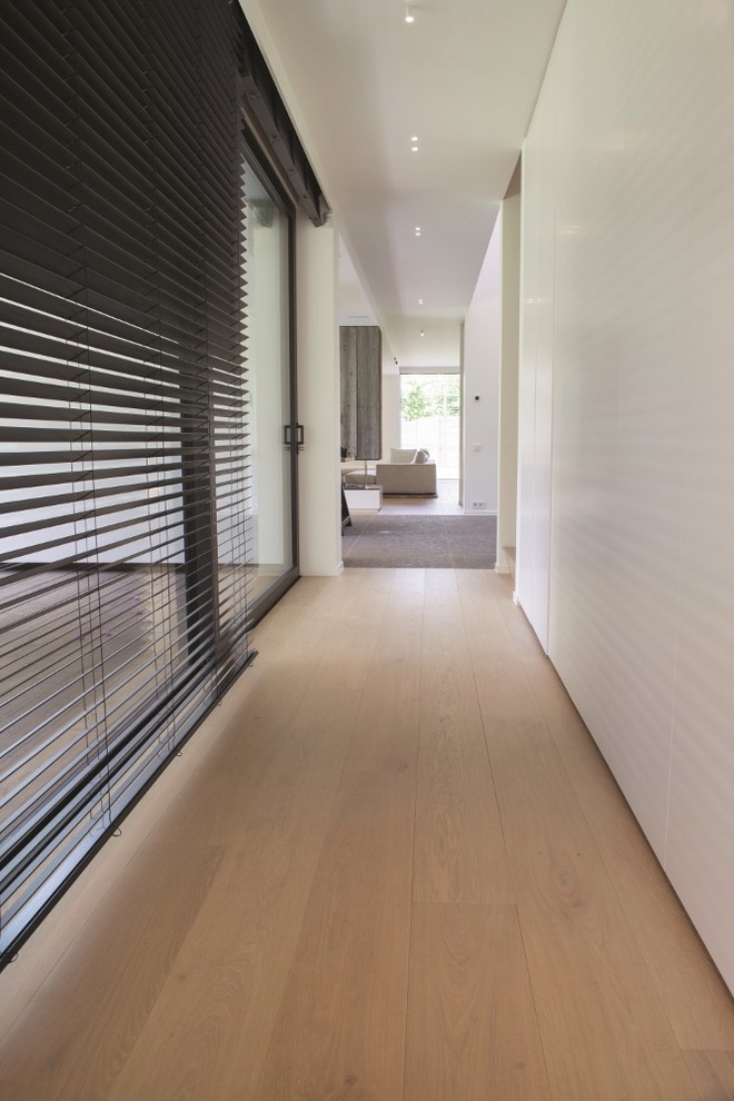 Idée de décoration pour un couloir minimaliste de taille moyenne avec parquet clair et un mur blanc.