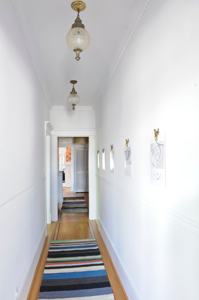 Diseño de recibidores y pasillos eclécticos con paredes blancas y suelo de madera en tonos medios
