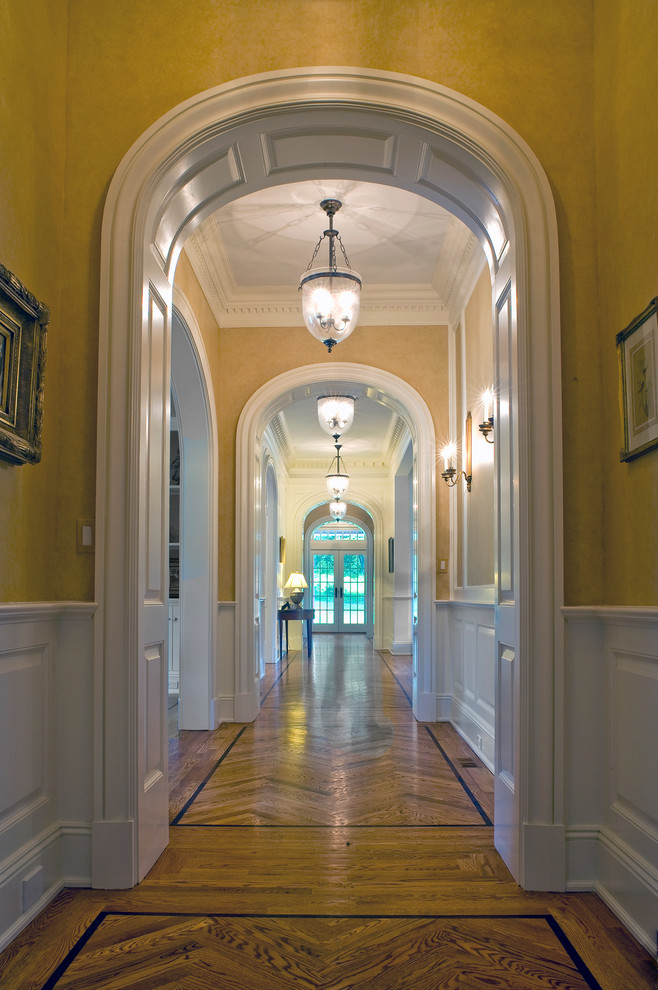 Cette photo montre un grand couloir chic avec un mur jaune et parquet clair.