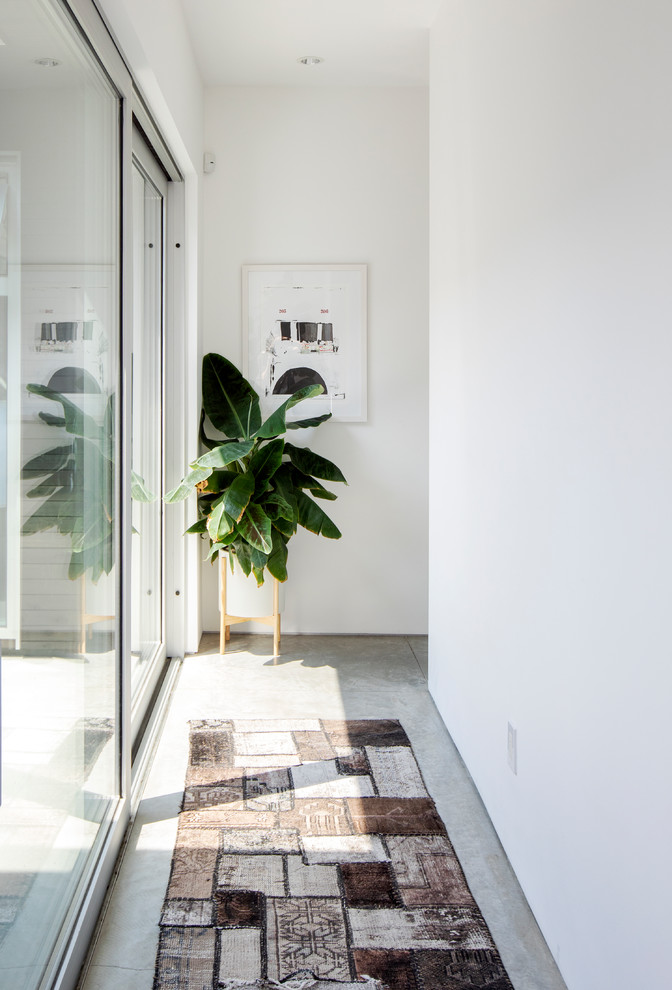 Cette image montre un couloir minimaliste de taille moyenne avec un mur blanc, sol en béton ciré et un sol gris.