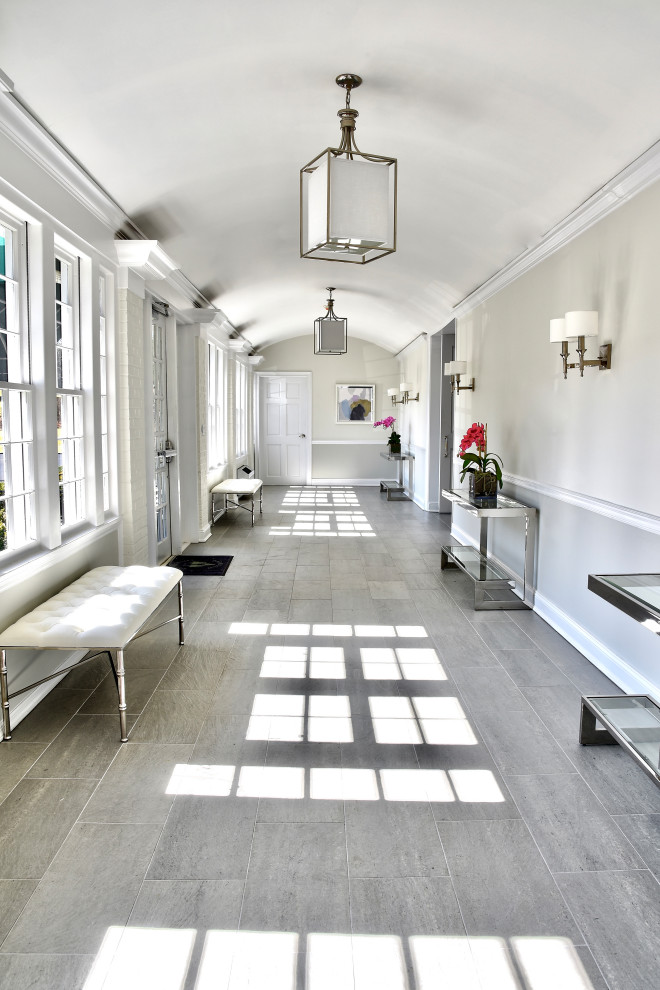 На фото: огромный коридор в стиле неоклассика (современная классика) с серыми стенами, полом из керамической плитки и серым полом