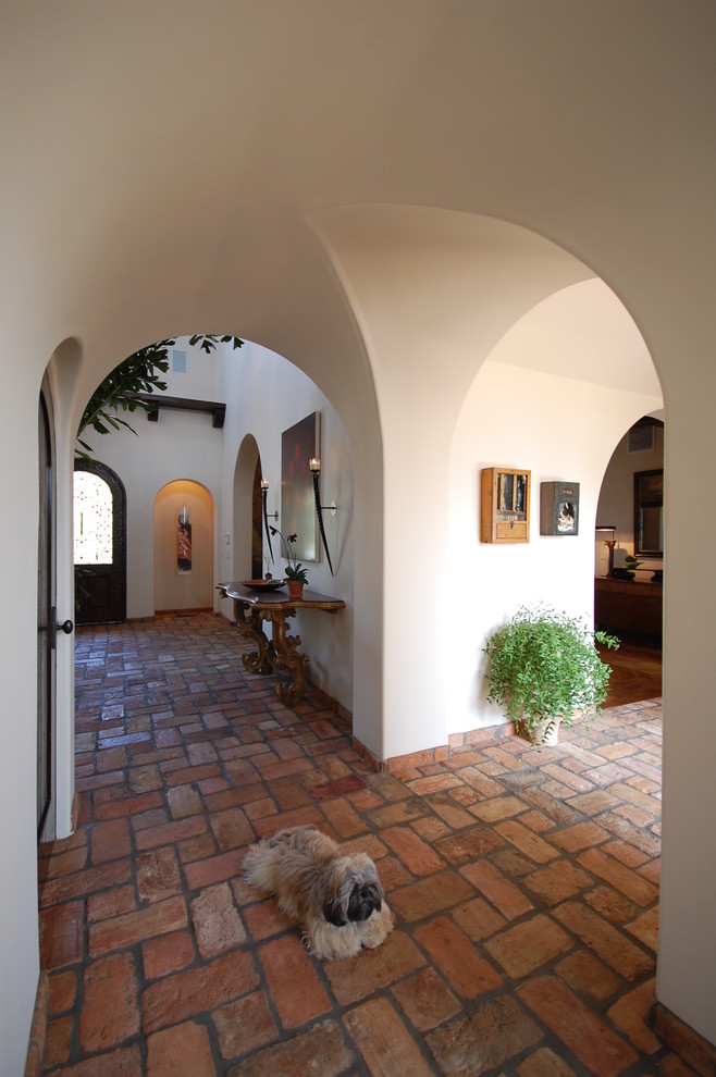 На фото: большой коридор в средиземноморском стиле с белыми стенами и кирпичным полом с