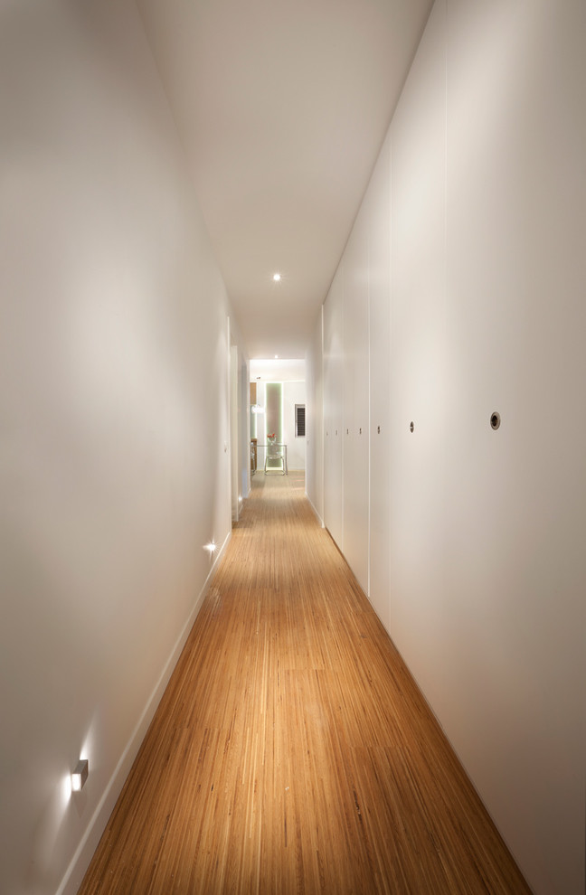Cette photo montre un couloir moderne avec un mur blanc et un sol en bois brun.