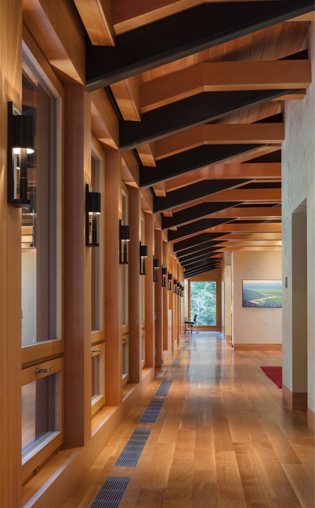 Aménagement d'un grand couloir moderne avec un mur beige, un sol en bois brun et un sol marron.