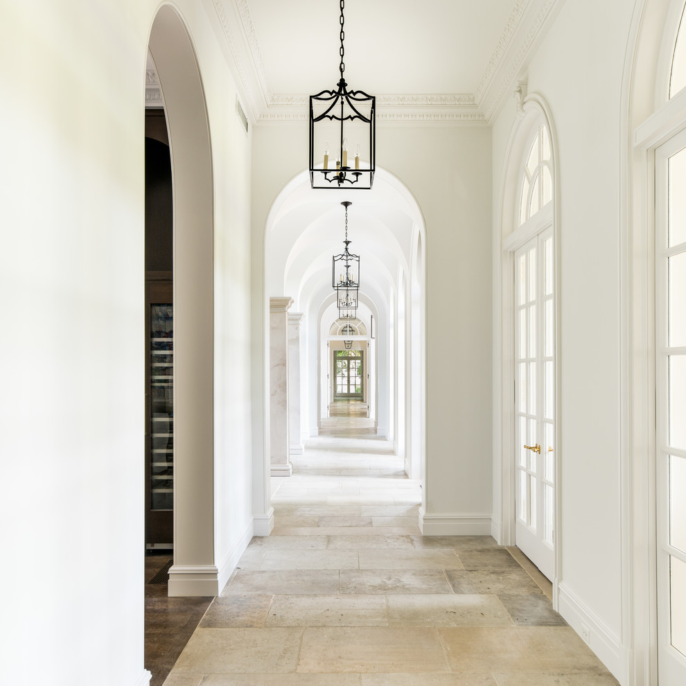 Пример оригинального дизайна: большой коридор в стиле неоклассика (современная классика) с белыми стенами, полом из известняка и бежевым полом