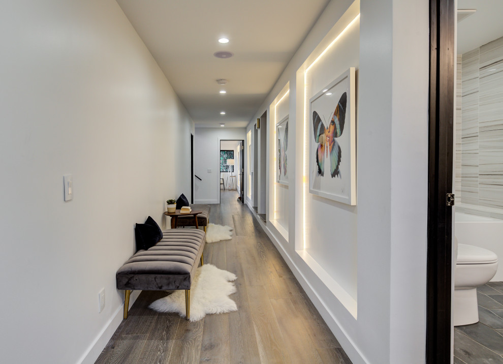 Cette photo montre un grand couloir tendance avec un mur blanc, un sol en bois brun et un sol noir.