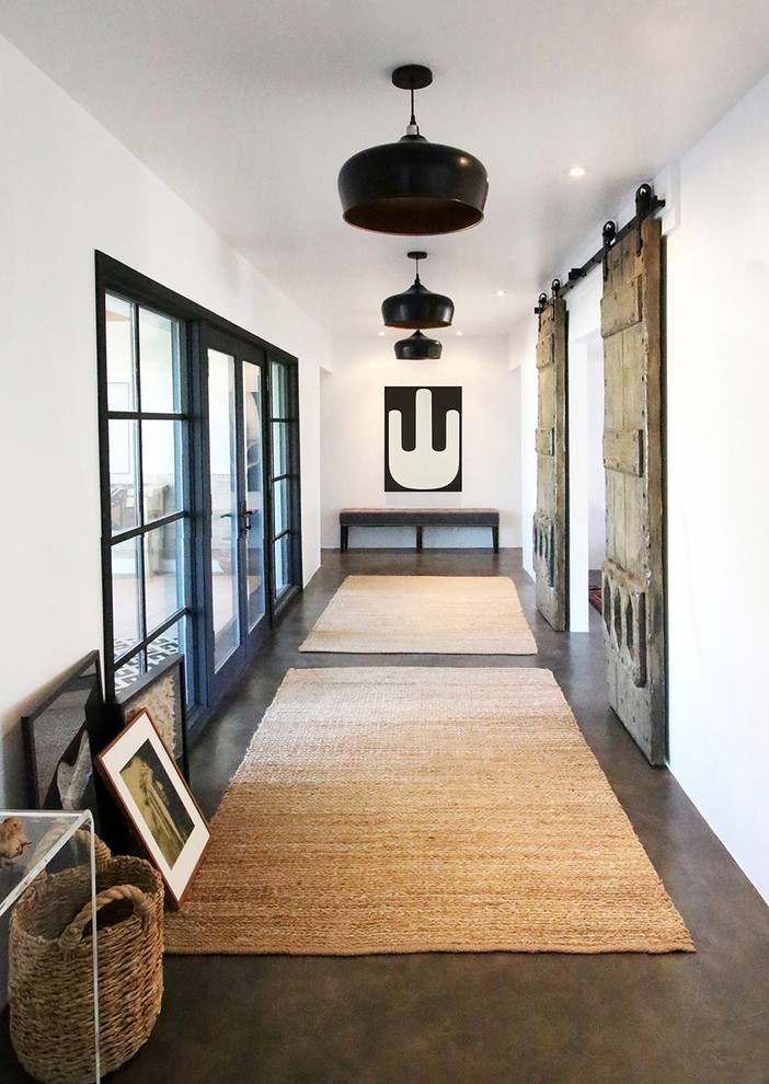 Immagine di un ingresso o corridoio country con pareti bianche, pavimento in cemento e pavimento marrone