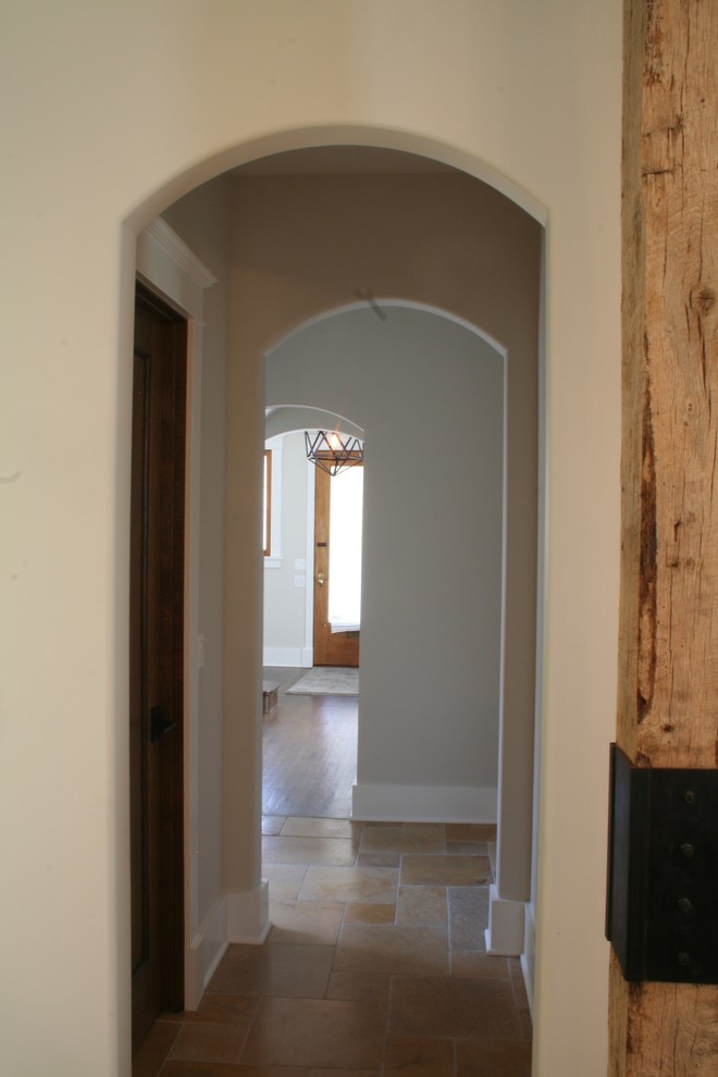 На фото: коридор среднего размера в стиле неоклассика (современная классика) с бежевыми стенами, полом из травертина и коричневым полом с