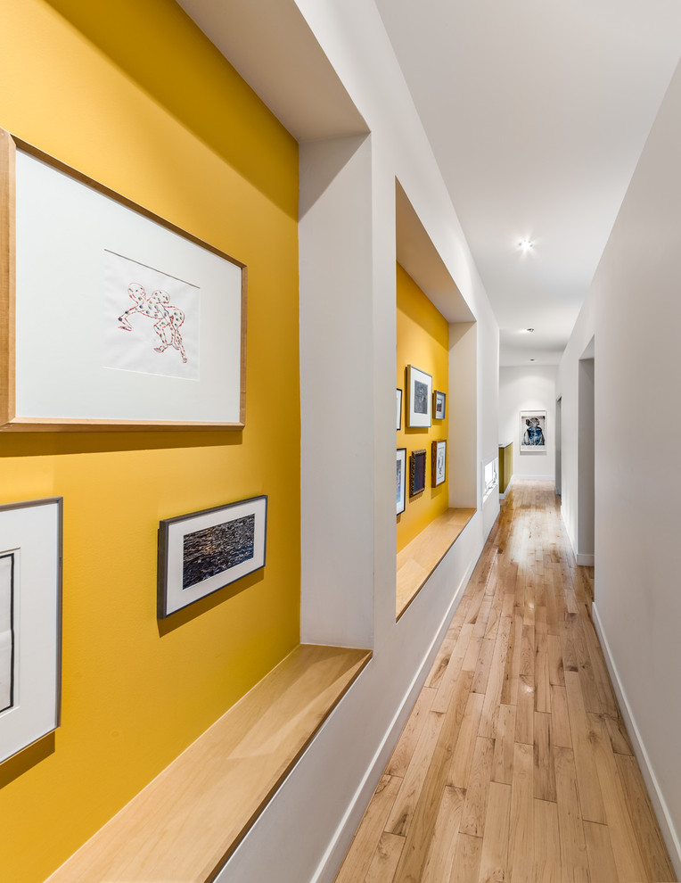 Réalisation d'un couloir design avec un mur jaune, parquet clair et un sol beige.