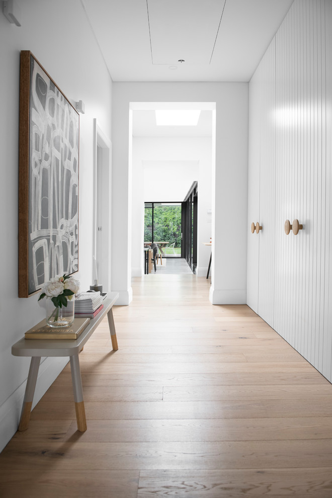 Réalisation d'un grand couloir minimaliste avec un mur blanc et parquet clair.