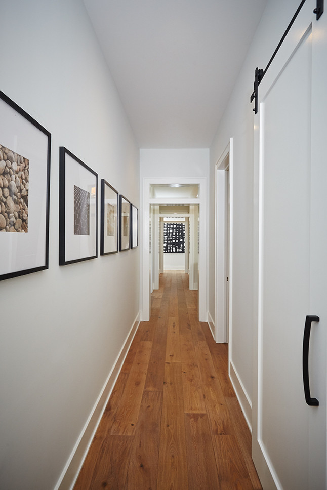 Réalisation d'un grand couloir champêtre avec un mur gris et un sol en bois brun.