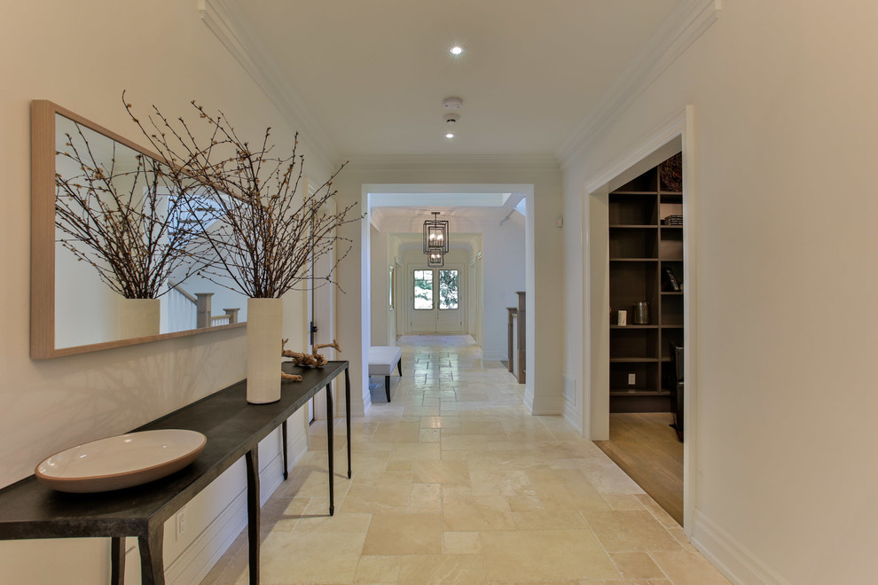 Пример оригинального дизайна: большой коридор в стиле неоклассика (современная классика) с белыми стенами и полом из известняка