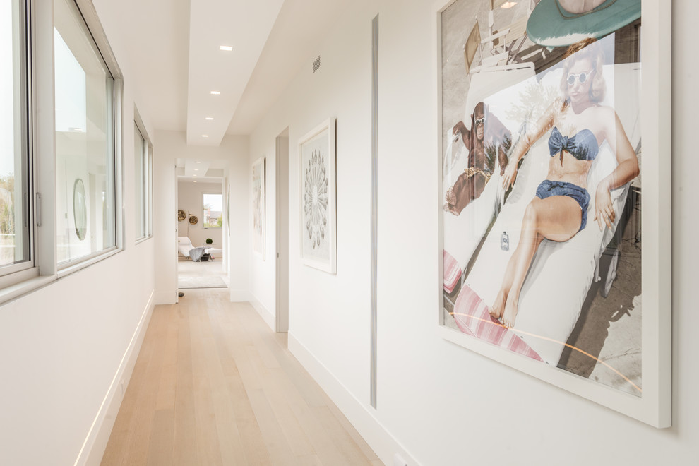 Réalisation d'un couloir design avec un mur blanc, parquet clair et un sol beige.
