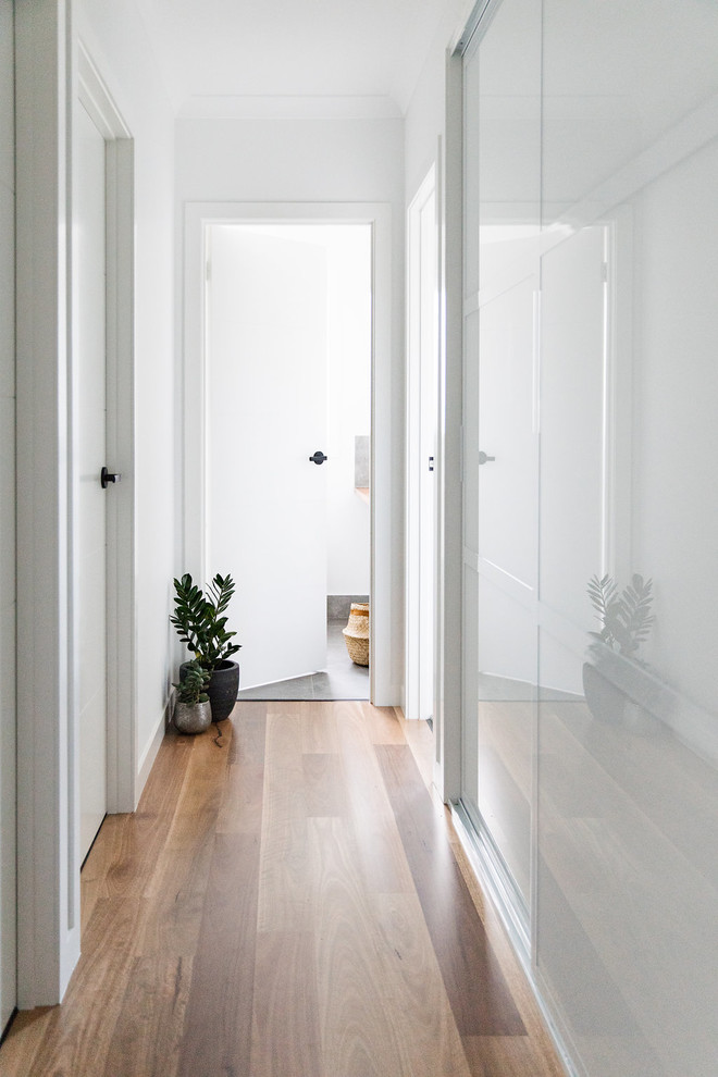 Diseño de recibidores y pasillos minimalistas con paredes blancas, suelo de madera en tonos medios y suelo marrón