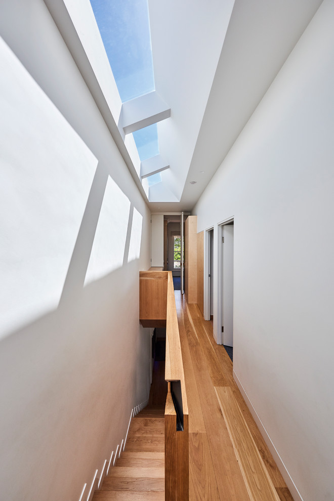Réalisation d'un couloir design de taille moyenne avec un mur blanc et un sol en bois brun.