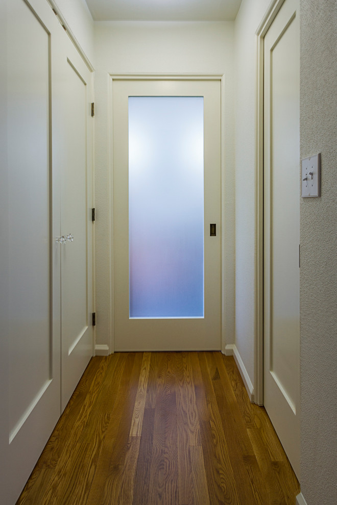 Aménagement d'un petit couloir éclectique avec un mur blanc, un sol en bois brun et un sol marron.