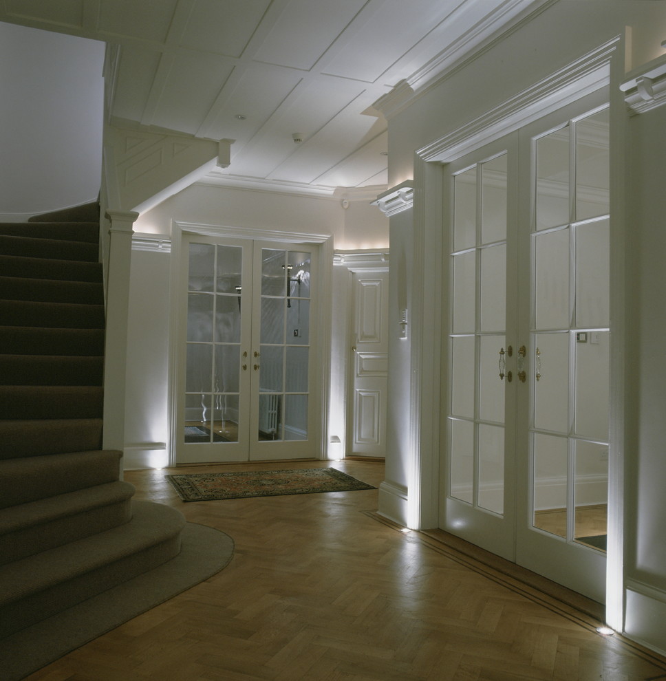 На фото: большой коридор в классическом стиле с белыми стенами и паркетным полом среднего тона с