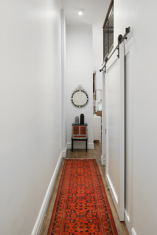 Cette image montre un petit couloir traditionnel avec un mur blanc, un sol en bois brun et un sol marron.