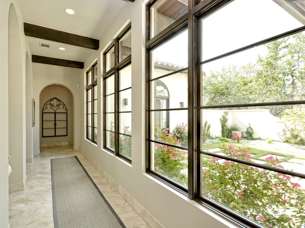 На фото: большой коридор в стиле неоклассика (современная классика) с белыми стенами и полом из травертина с