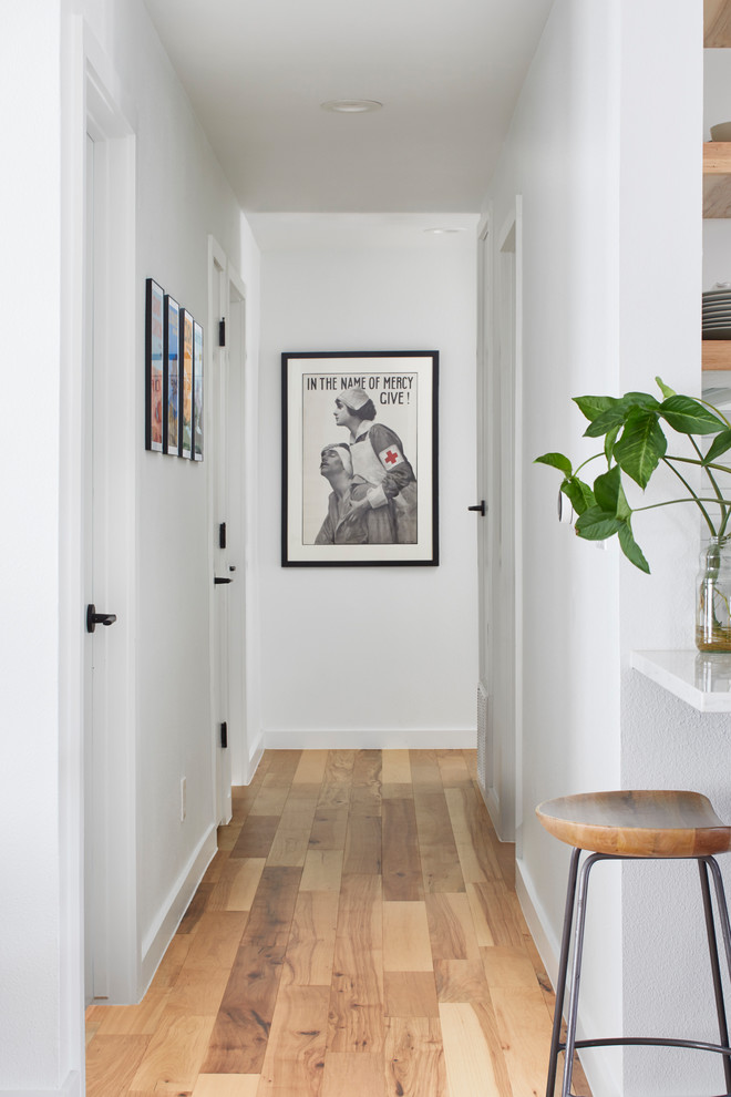 Cette image montre un couloir minimaliste de taille moyenne avec un mur blanc, parquet clair et un sol marron.