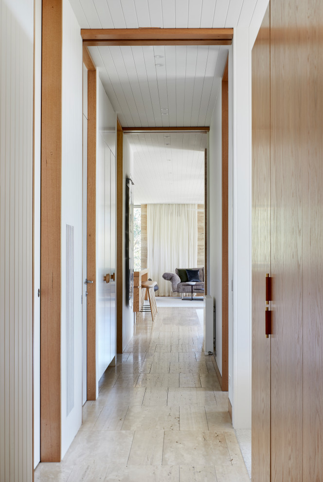 Exemple d'un grand couloir bord de mer avec un mur blanc, un sol en travertin, un sol beige et un plafond en lambris de bois.