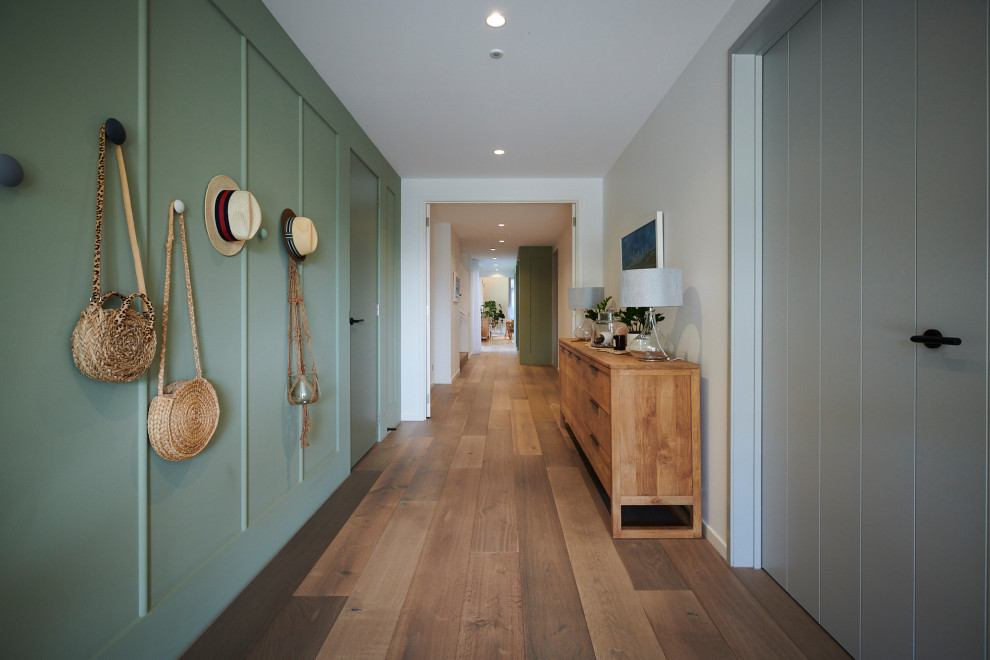 Aménagement d'un grand couloir contemporain avec un mur vert, un sol en bois brun et un sol marron.