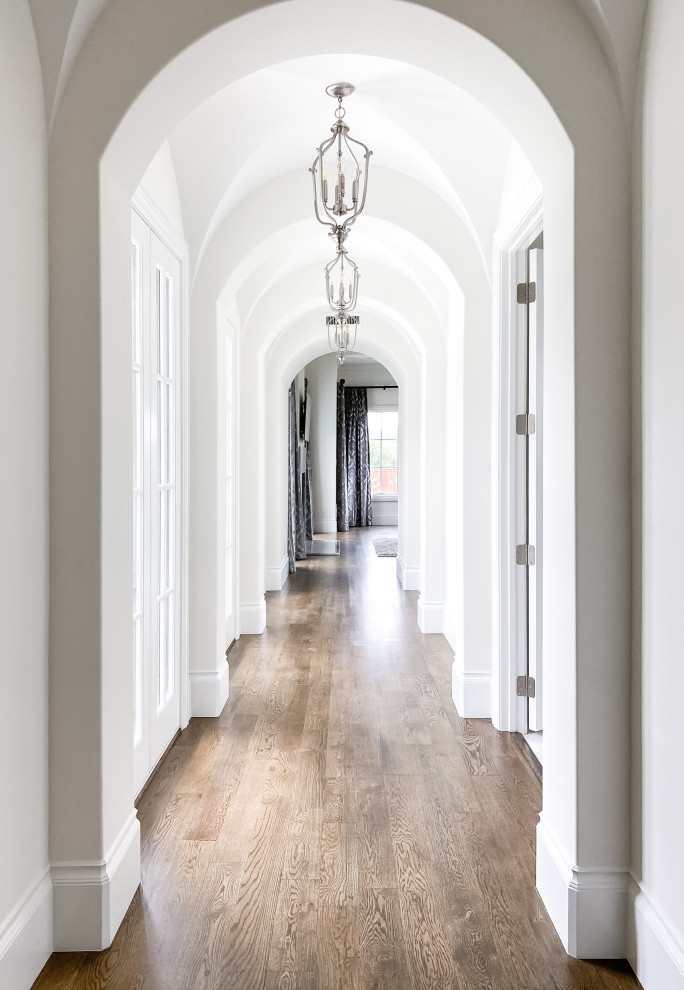 Aménagement d'un très grand couloir moderne avec un mur blanc, parquet foncé, un sol marron et un plafond voûté.