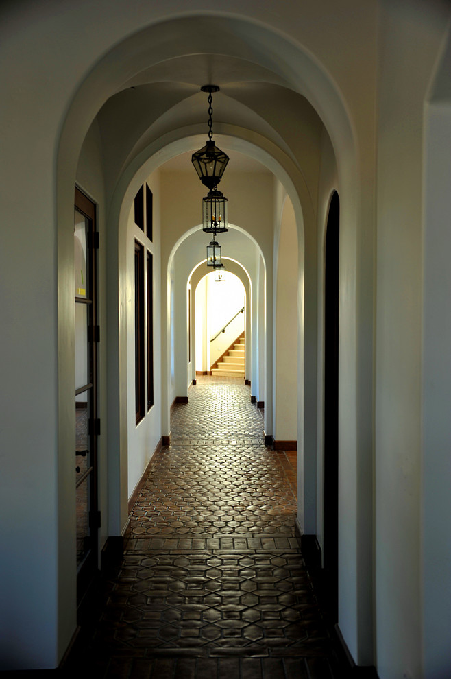 На фото: большой коридор в средиземноморском стиле с белыми стенами, полом из терракотовой плитки и красным полом с