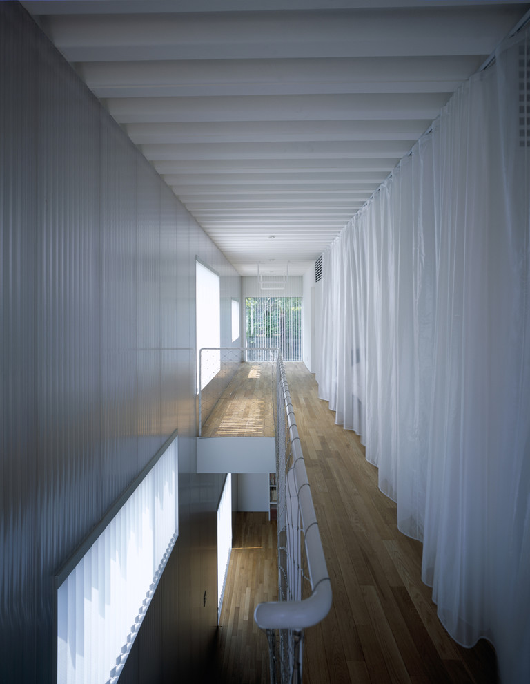 Réalisation d'un couloir design avec un mur blanc et un sol en bois brun.