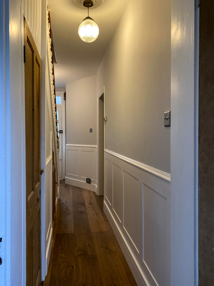 На фото: коридор среднего размера в стиле неоклассика (современная классика) с паркетным полом среднего тона и панелями на части стены с