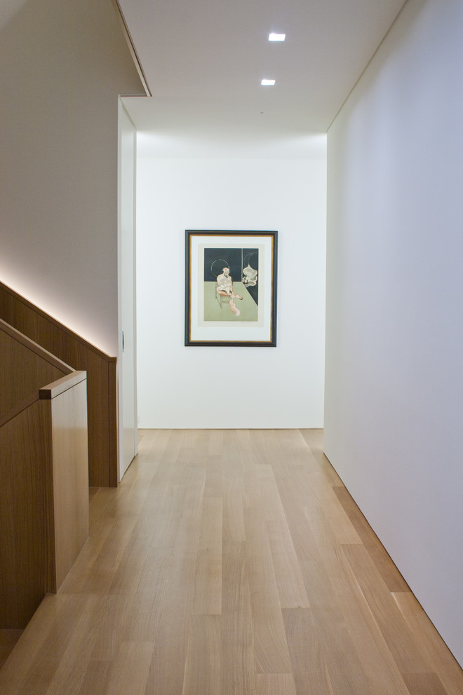 Cette photo montre un grand couloir moderne avec un mur blanc et un sol en bois brun.