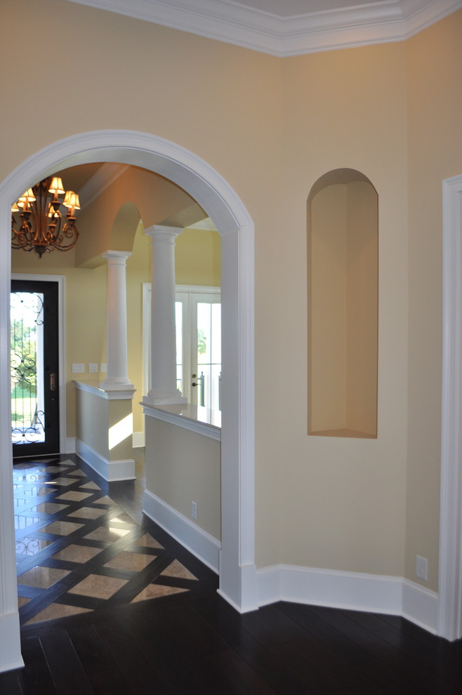 Aménagement d'un grand couloir classique avec un mur beige, parquet foncé et un sol multicolore.