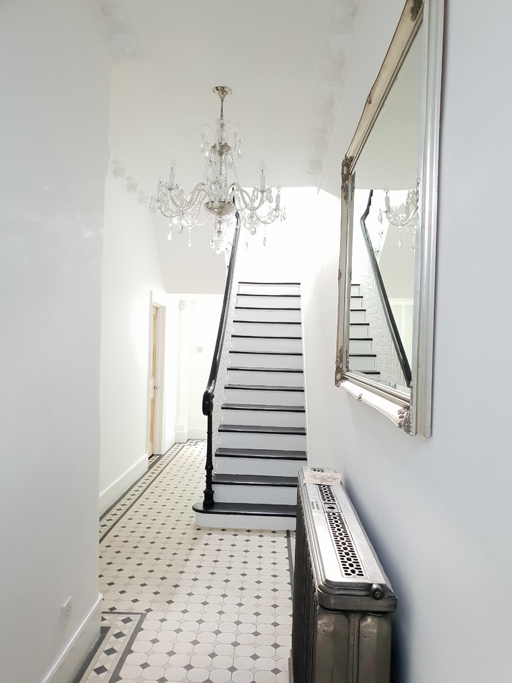 Стильный дизайн: огромный коридор в классическом стиле с белыми стенами, темным паркетным полом, черным полом и многоуровневым потолком - последний тренд