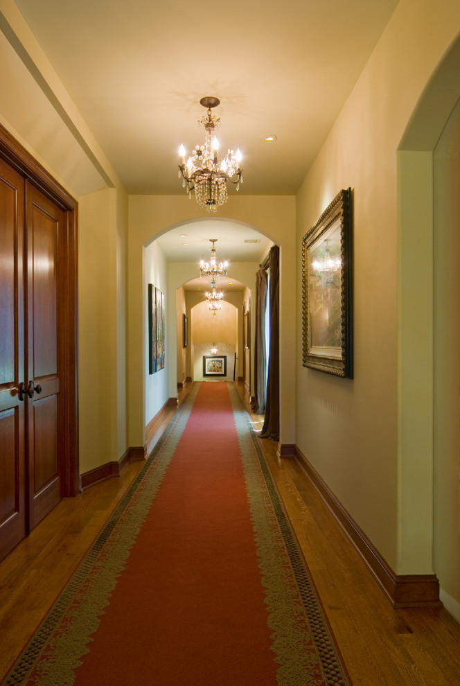 Cette image montre un grand couloir traditionnel avec un sol en bois brun et un mur beige.