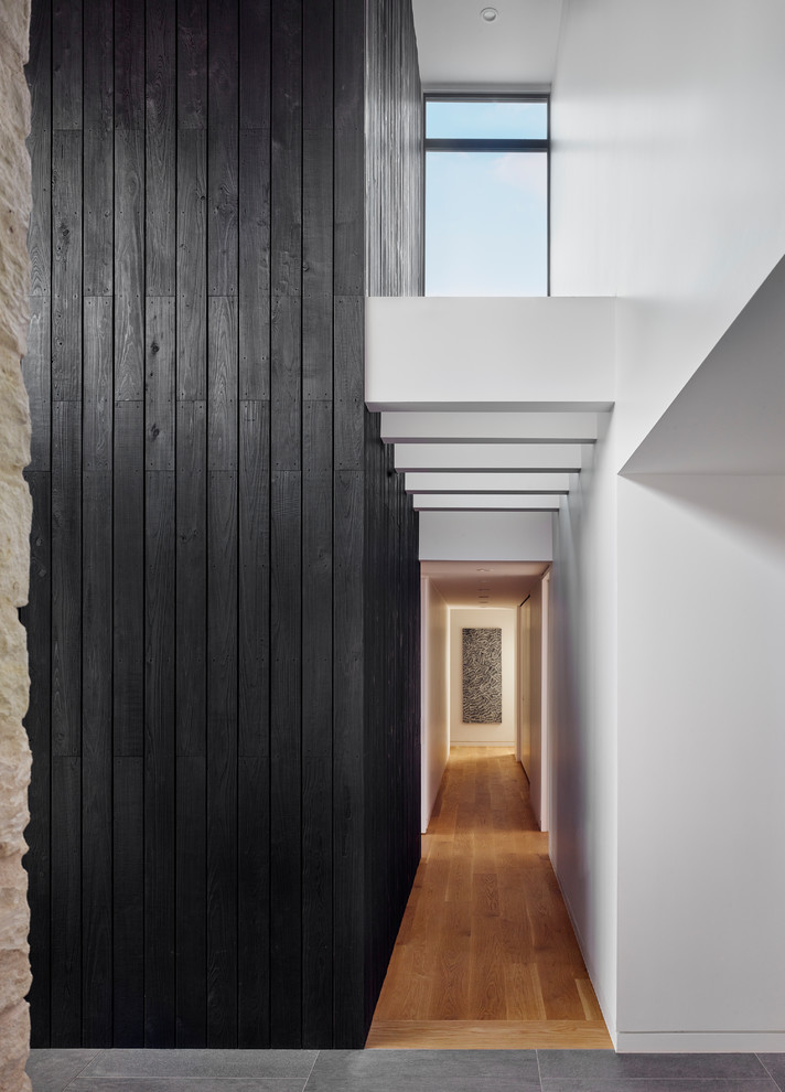 Diseño de recibidores y pasillos actuales con paredes negras, suelo de madera en tonos medios, suelo marrón y cuadros