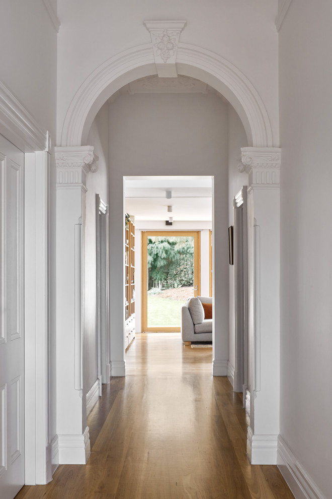Ispirazione per un grande ingresso o corridoio minimal con pareti bianche, pavimento in legno massello medio, pavimento marrone e boiserie