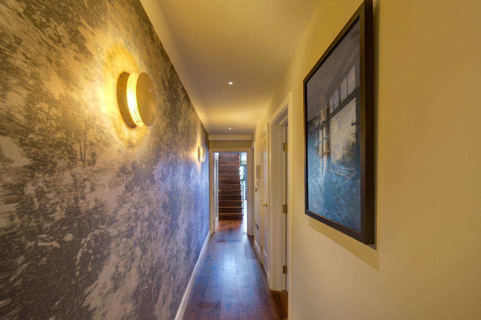 Example of a mid-sized trendy medium tone wood floor, brown floor, tray ceiling and wallpaper hallway design in London with multicolored walls