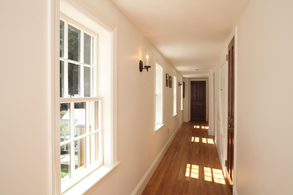 Cette image montre un couloir traditionnel avec un mur blanc et un sol en bois brun.