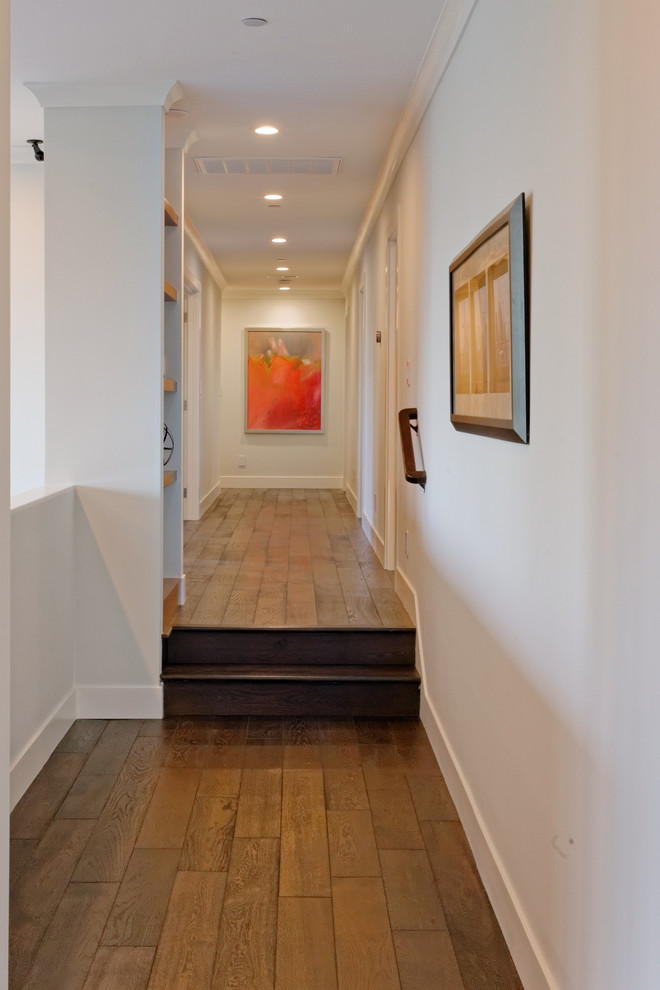 Cette photo montre un grand couloir moderne avec un mur blanc, un sol marron et parquet foncé.