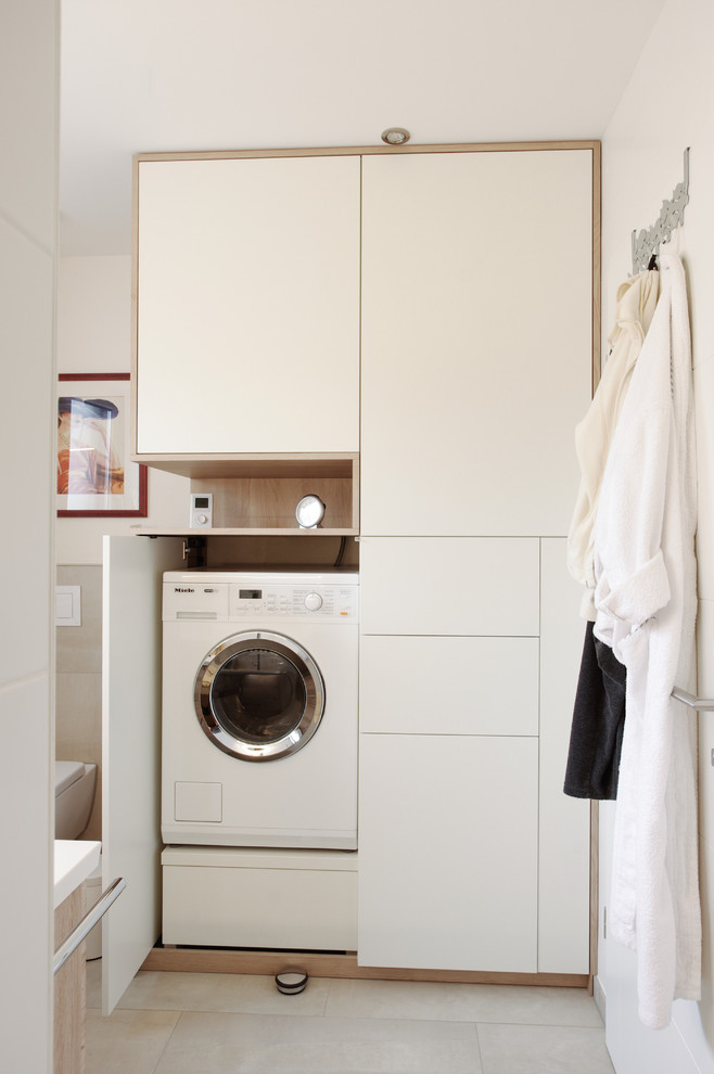 Inspiration för små moderna linjära tvättstugor enbart för tvätt, med släta luckor, träbänkskiva, beige väggar, klinkergolv i keramik, tvättmaskin och torktumlare byggt in i ett skåp, svart golv och vita skåp