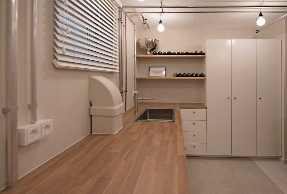 Inspiration for a mid-sized u-shaped ceramic tile and gray floor dedicated laundry room remodel in Munich with a drop-in sink, flat-panel cabinets, white cabinets, laminate countertops, beige walls, a side-by-side washer/dryer and brown countertops