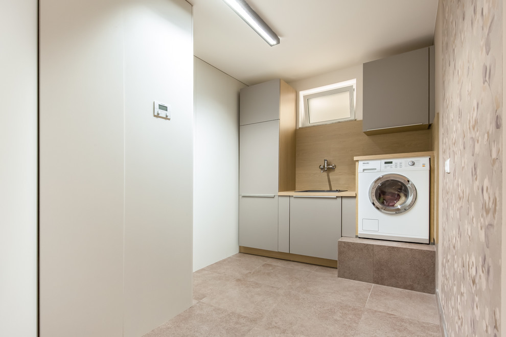 Immagine di una piccola lavanderia multiuso design con lavello sottopiano, ante lisce, pareti beige, pavimento in pietra calcarea e ante grigie