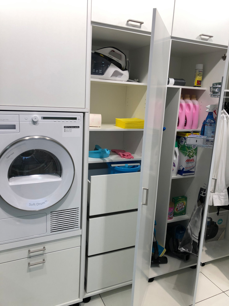 This is an example of a large contemporary single-wall utility room in Other with flat-panel cabinets, white cabinets, an integrated washer and dryer and white floors.