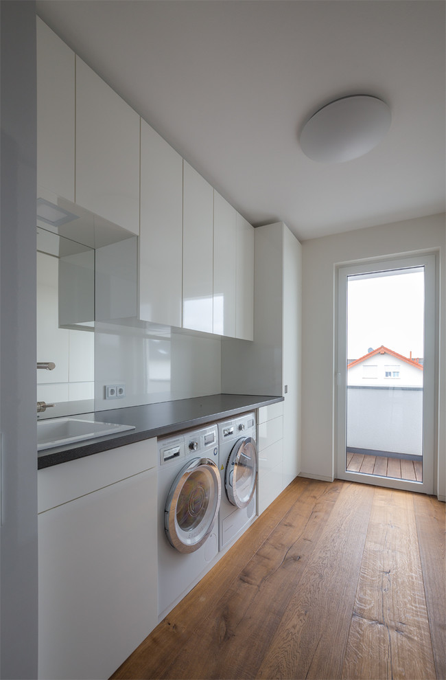 Diseño de lavadero minimalista con puertas de armario blancas, paredes blancas y suelo de madera pintada